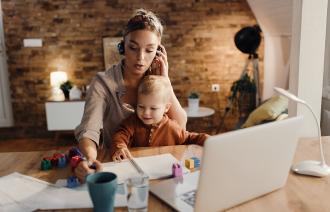Frau mit Kind telefoniert vor ihrem Laptop